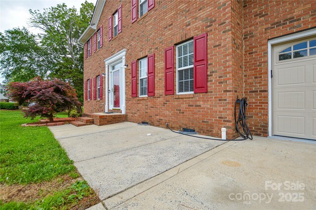 entrance to property featuring brick siding, driveway, and crawl space