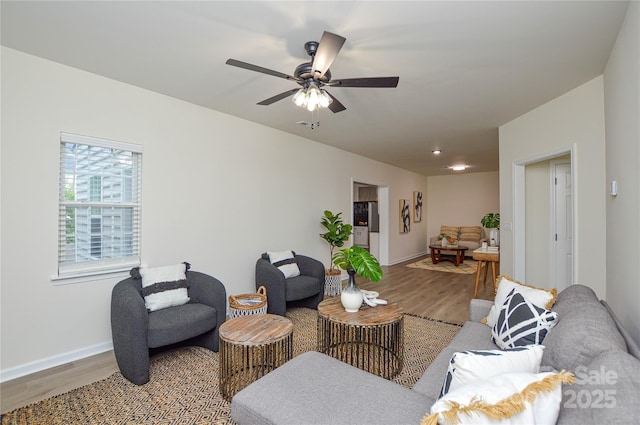 living area featuring wood finished floors, baseboards, and a ceiling fan