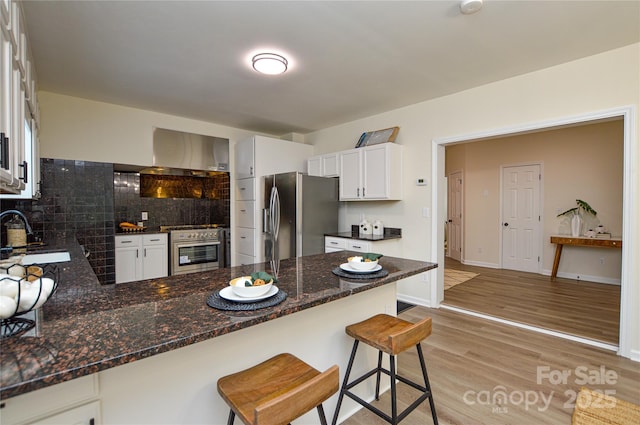 kitchen with stainless steel appliances, a sink, decorative backsplash, a peninsula, and light wood-style floors