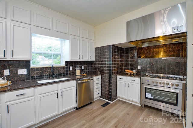kitchen featuring stainless steel appliances, wall chimney exhaust hood, a sink, white cabinetry, and light wood-style flooring