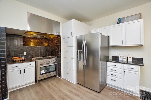 kitchen featuring stainless steel appliances, wall chimney range hood, light wood-style flooring, and dark stone counters