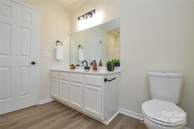 bathroom with wood finished floors, baseboards, toilet, and vanity