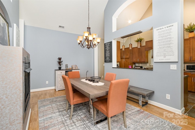 14807 Middlesborough Dr, Matthews, NC 28104 - dining space featuring a chandelier, light wood-style floors, a fireplace, vaulted ceiling, and baseboards