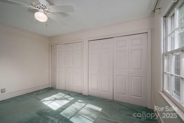unfurnished bedroom featuring carpet floors, ornamental molding, two closets, baseboards, and a ceiling fan