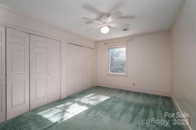unfurnished bedroom with crown molding, visible vents, two closets, baseboards, and carpet