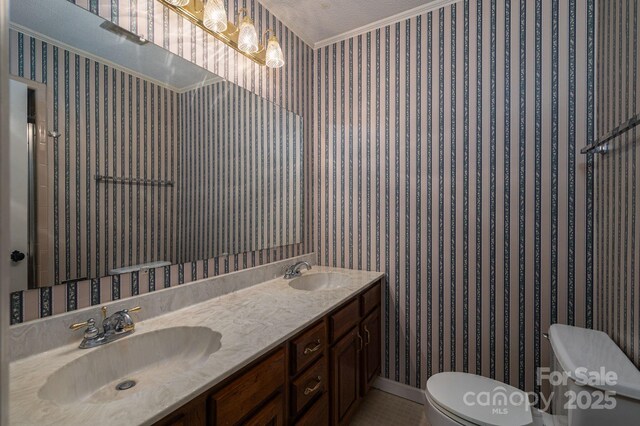 bathroom with double vanity, a sink, toilet, and ornamental molding