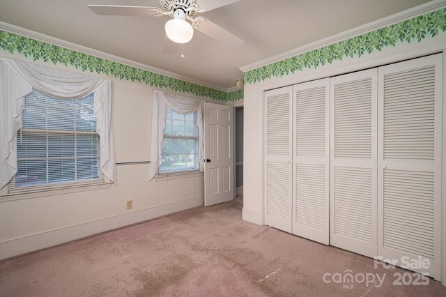unfurnished bedroom featuring a ceiling fan, baseboards, a closet, ornamental molding, and carpet flooring