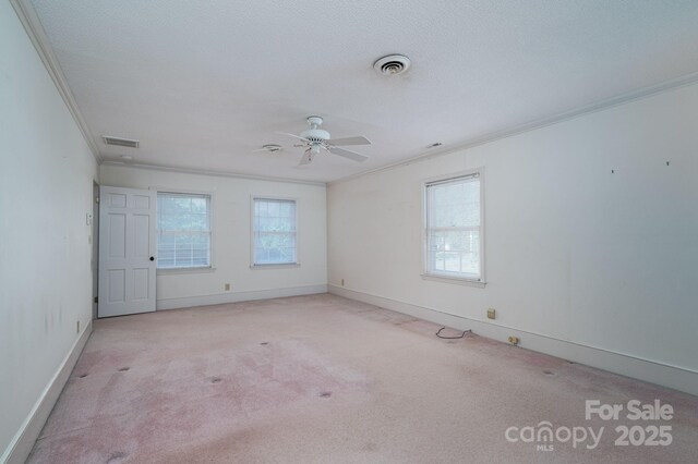 carpeted spare room featuring crown molding, ceiling fan, visible vents, and baseboards