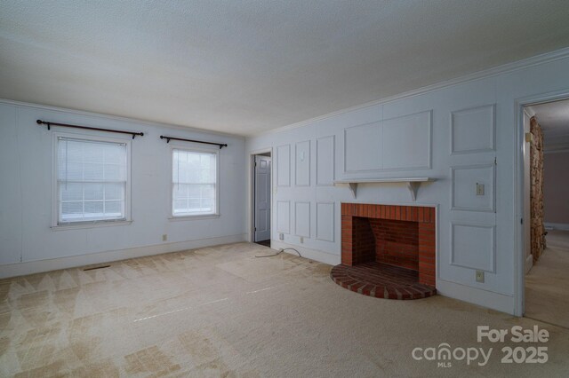 unfurnished living room with a brick fireplace, baseboards, ornamental molding, and light carpet