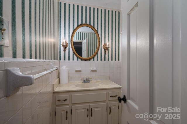 bathroom with tile walls, a wainscoted wall, vanity, and wallpapered walls