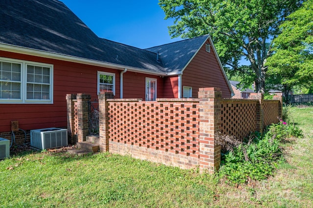 view of home's exterior featuring central air condition unit, fence, a lawn, and roof with shingles