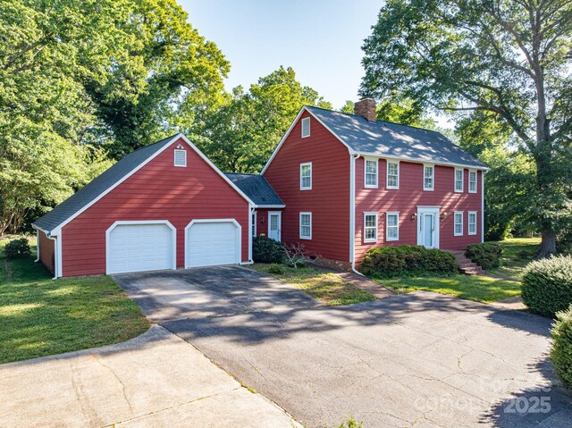 colonial-style house with a garage, a chimney, a front lawn, and aphalt driveway