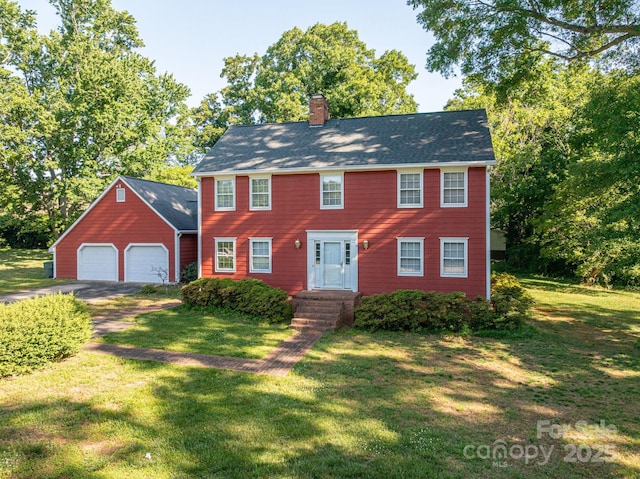 colonial-style house with an attached garage, a front lawn, aphalt driveway, and a chimney