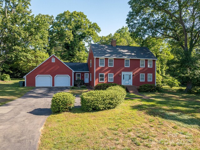 colonial-style house featuring a garage, aphalt driveway, a front yard, and a chimney