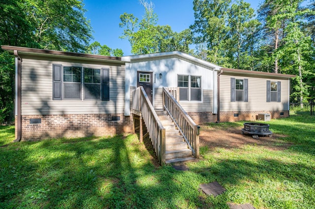 manufactured / mobile home with a front yard, a fire pit, central AC, and crawl space