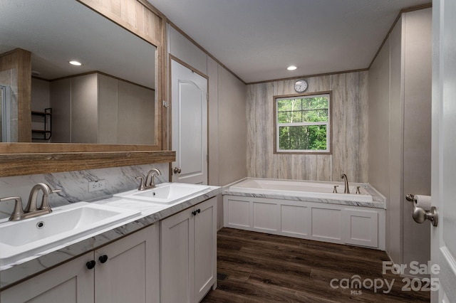 bathroom with a garden tub, crown molding, a sink, and wood finished floors