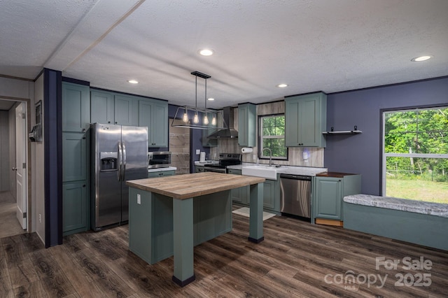 kitchen featuring wooden counters, appliances with stainless steel finishes, a sink, wall chimney exhaust hood, and dark wood-style flooring