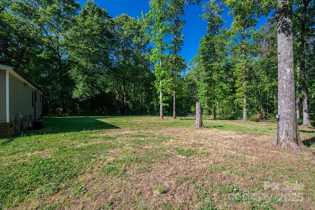 view of grassy yard with central AC and a wooded view