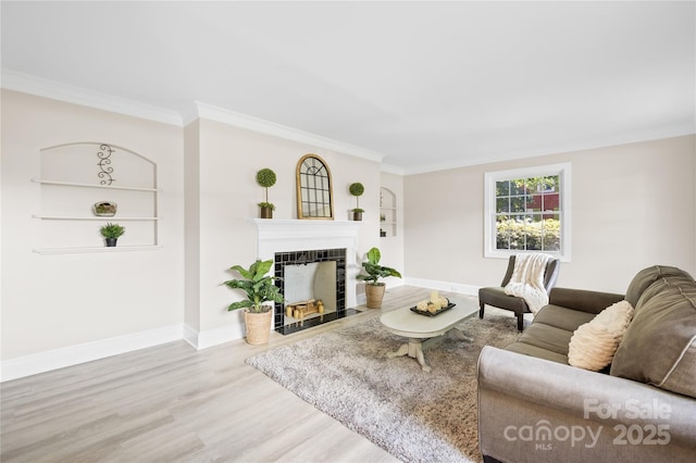 living area with wood finished floors, ornamental molding, baseboards, a tiled fireplace, and built in shelves