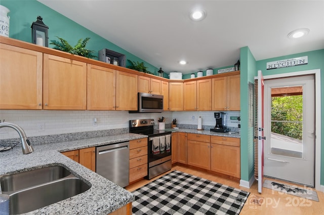 kitchen with decorative backsplash, appliances with stainless steel finishes, light stone countertops, a sink, and light wood-style flooring