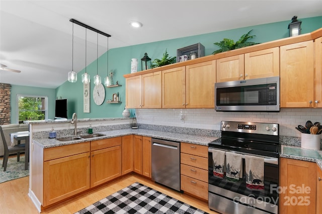 kitchen with appliances with stainless steel finishes, a sink, a peninsula, lofted ceiling, and light wood-style floors
