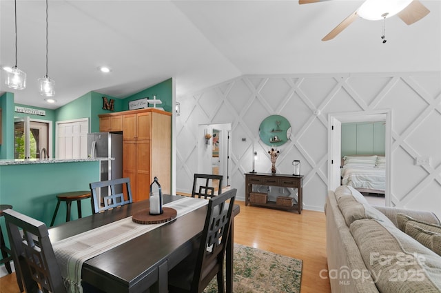 dining room with vaulted ceiling, a decorative wall, a ceiling fan, and light wood-style flooring