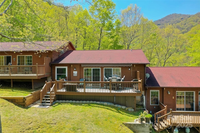 back of property with a lawn, roof with shingles, and a deck