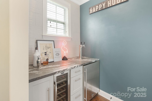 bar featuring decorative backsplash, stainless steel refrigerator, baseboards, a bar, and beverage cooler