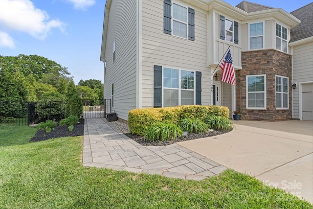 view of property exterior featuring fence, stone siding, a gate, a lawn, and driveway