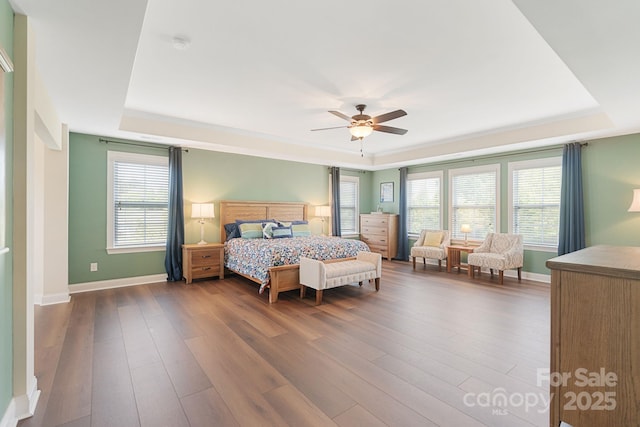 bedroom with baseboards, a ceiling fan, a tray ceiling, and dark wood-style flooring