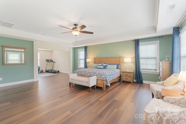 bedroom with a raised ceiling, baseboards, wood finished floors, and visible vents
