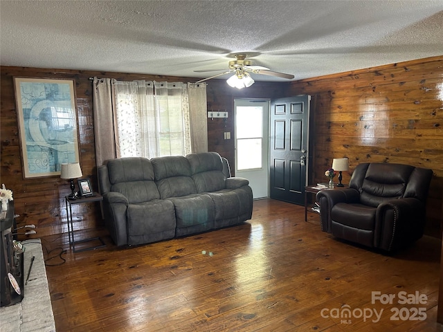 living room with wood-type flooring, a ceiling fan, a textured ceiling, and wood walls