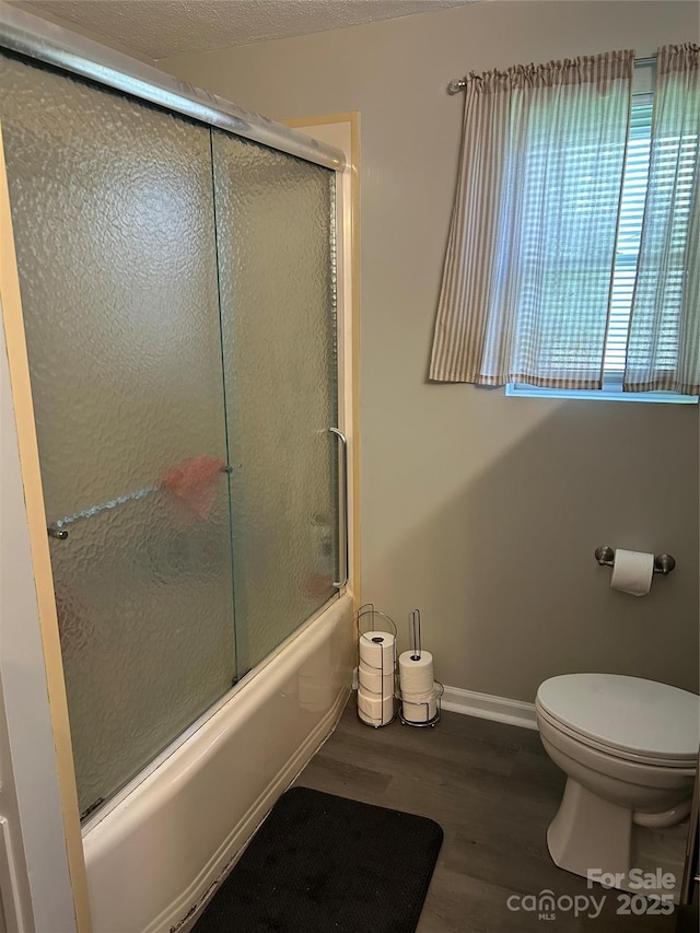 bathroom featuring baseboards, enclosed tub / shower combo, toilet, and wood finished floors