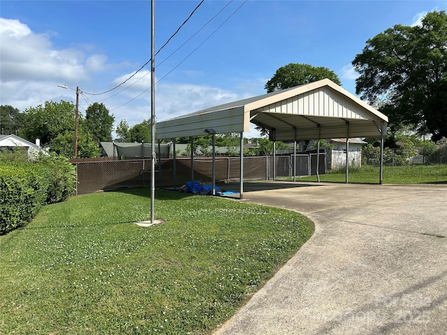 view of parking / parking lot featuring concrete driveway, fence, and a carport