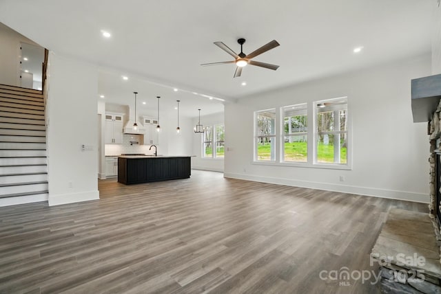 unfurnished living room featuring a sink, wood finished floors, baseboards, stairway, and a ceiling fan