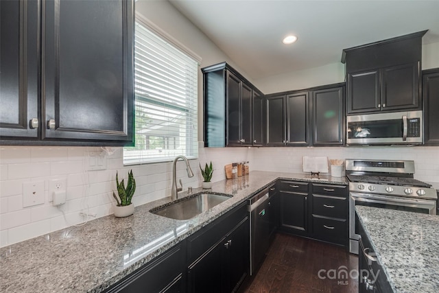 kitchen with dark wood-style flooring, light stone countertops, appliances with stainless steel finishes, a sink, and dark cabinets