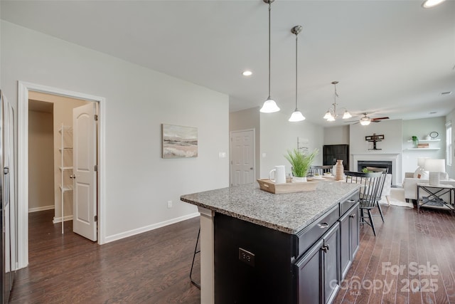kitchen featuring dark wood-style flooring, a breakfast bar, a fireplace, ceiling fan, and light stone counters
