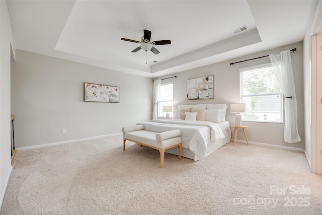 bedroom featuring visible vents, baseboards, a tray ceiling, and multiple windows