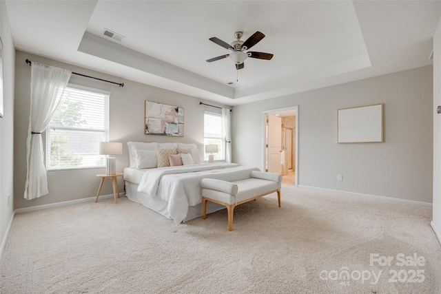 carpeted bedroom with a ceiling fan, visible vents, a raised ceiling, baseboards, and connected bathroom