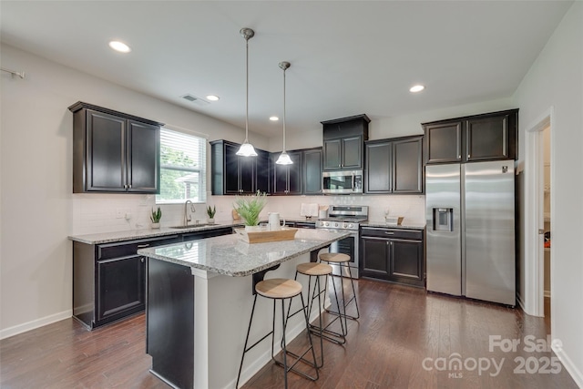 kitchen with visible vents, a center island, light stone counters, a sink, and stainless steel appliances