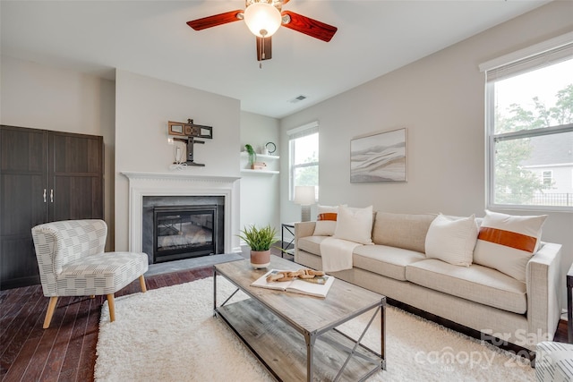 living area with visible vents, a glass covered fireplace, ceiling fan, and wood finished floors