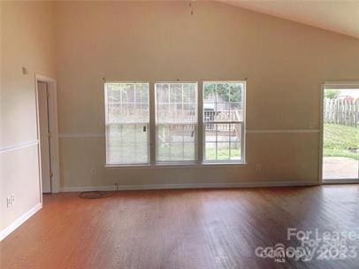 unfurnished room featuring baseboards, high vaulted ceiling, and wood finished floors