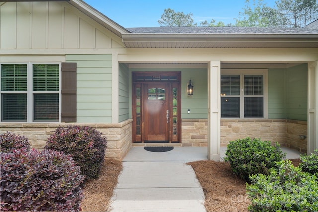 entrance to property featuring stone siding, a shingled roof, and board and batten siding
