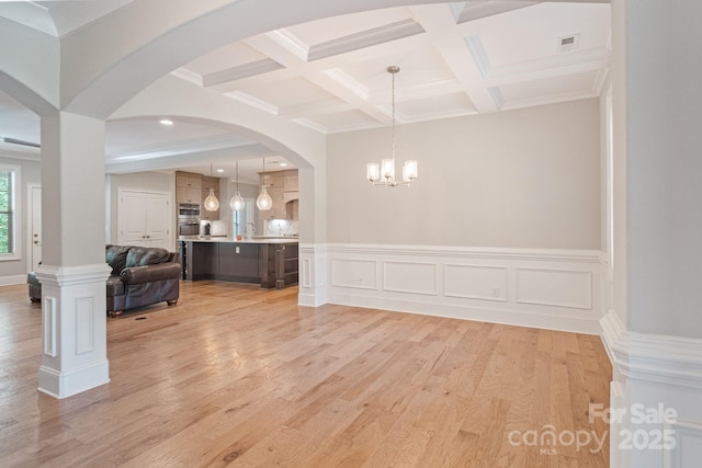 unfurnished dining area featuring coffered ceiling, light wood-type flooring, a chandelier, arched walkways, and beam ceiling