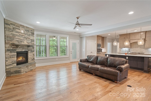 living room with ornamental molding, ceiling fan, baseboards, light wood-style flooring, and a stone fireplace