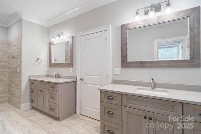 bathroom featuring two vanities, tiled shower, marble finish floors, and ornamental molding
