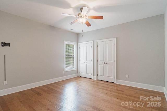 unfurnished bedroom featuring two closets, light wood-type flooring, baseboards, and ceiling fan