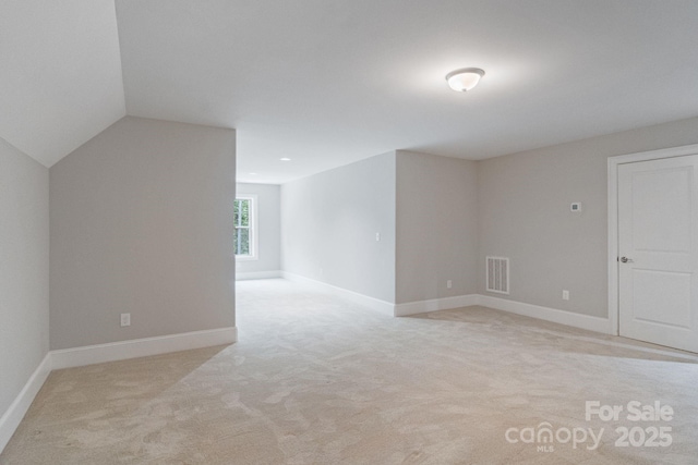spare room featuring light carpet, lofted ceiling, and baseboards