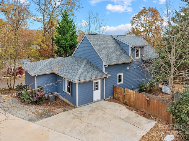 view of side of property featuring fence, cooling unit, and roof with shingles