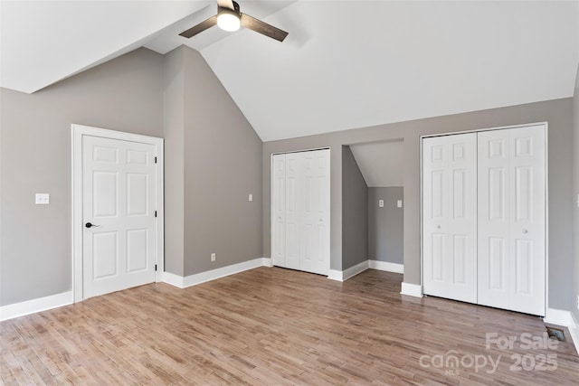 unfurnished bedroom featuring two closets, baseboards, vaulted ceiling, and light wood-style floors